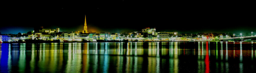 night time shot of Wexford town quay side from the far side of the Slaney River. the town is lit up in a variety of colours