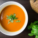 Delicious homemade tomato soup served with basil leaves and rustic bread.